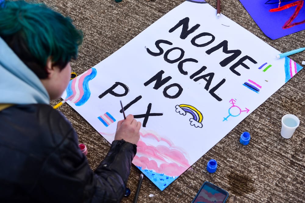Pessoa pintando um cartaz com os dizeres "Nome social no Pix" durante ação na Praça da Gare
